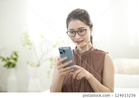 年輕女子坐在床上，看著她的智能手機 124013256