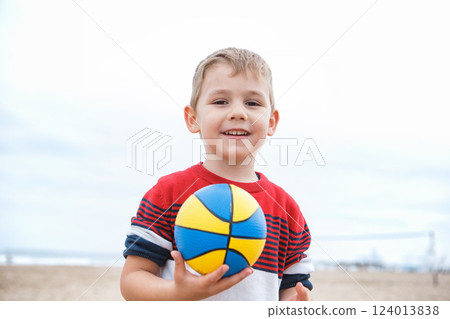Young Boy Playing With a Colorful Beach Ball on a Sandy Shoreline During a Cloudy Afternoon 124013838