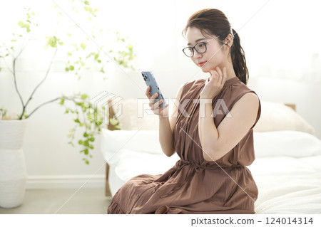 Young woman sitting in bed and looking at her smartphone 124014314