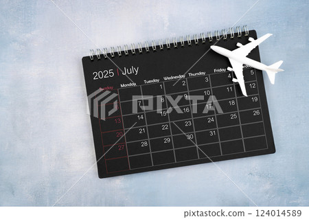 July 2025 black calendar and airplane toy on wooden table. 124014589