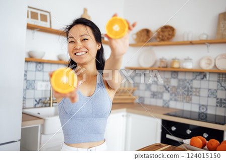 An attractive young Asian woman smiles and shows oranges to the camera. A beautiful Thai girl prepares a healthy breakfast with citrus fruits. 124015150