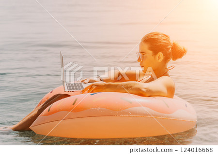 Woman Laptop Beach Work - Young woman working on laptop while floating on an inflatable ring in the ocean. Woman Laptop Beach Work - Young woman working on laptop while floating on an inflatable ring in the ocean. 124016668
