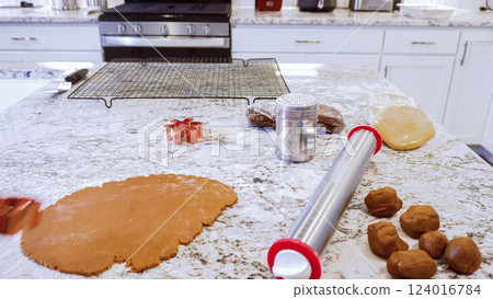 Using an adjustable rolling pin to roll out gingerbread cookie dough on the elegant marble counter in a modern kitchen, getting ready for festive holiday baking. 124016784