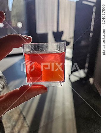 Hand Holding Small Square Plastic Cup with dessert Red jelly and fruit pieces . High quality photo Hand Holding Small Square Plastic Cup with dessert Red jelly and fruit pieces . High quality photo 124017006