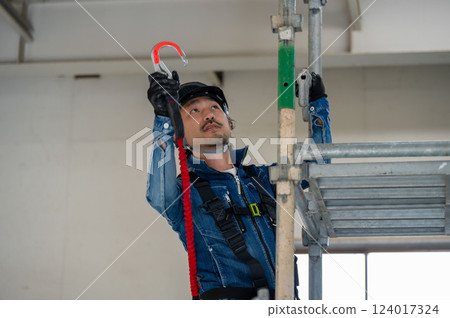 一名戴著安全帽的男子在鷹架上繫上安全帶 124017324
