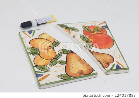 Cracked ceramic tile, broken into pieces, fragments of tiles, a tube of glue. 124017882