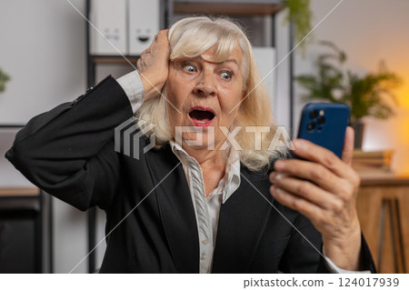 Surprised senior woman using smartphone typing browsing celebrating success victory at home office Surprised senior woman using smartphone typing browsing celebrating success victory at home office 124017939