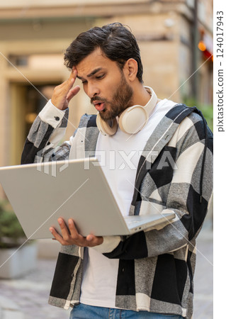 Shocked Indian man using laptop becoming surprised sudden lottery results bad news in city street 124017943