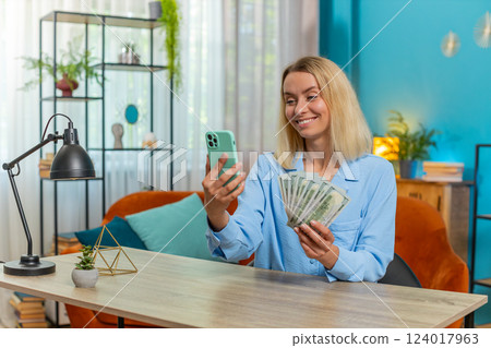 Happy rich businesswoman counting money dollar cash using smartphone calculator app at home office Happy rich businesswoman counting money dollar cash using smartphone calculator app at home office 124017963