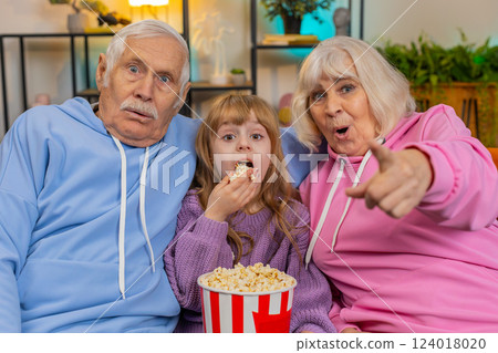 Child girl granddaughter grandfather grandmother eating popcorn watching movie film on home sofa Child girl granddaughter grandfather grandmother eating popcorn watching movie film on home sofa 124018020