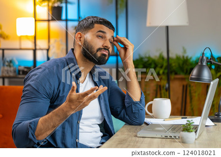 Overtired stressed tired Indian man freelancer bored with laptop while sitting at home office 124018021