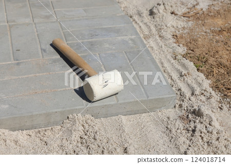 Rubber hammer on a gray pavement on the sand. Laying paving stones in city. 124018714
