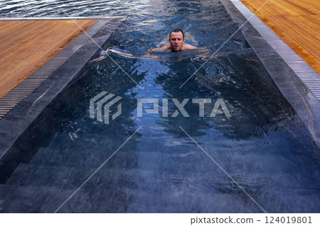 A young attractive man is swimming in an indoor pool. A handsome guy is relaxing 124019801