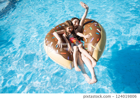 Two cute girls are swimming on an inflatable circle in the pool. A carefree teenager and her little sister are relaxing on vacation. Two cute girls are swimming on an inflatable circle in the pool. A carefree teenager and her little sister are relaxing on vacation. 124019806