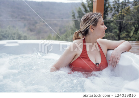 Close-up portrait of a young woman in a swimsuit relaxing in a Jacuzzi. An attractive blonde enjoys resting in the swirling water on vacation. Close-up portrait of a young woman in a swimsuit relaxing in a Jacuzzi. An attractive blonde enjoys resting in the swirling water on vacation. 124019810