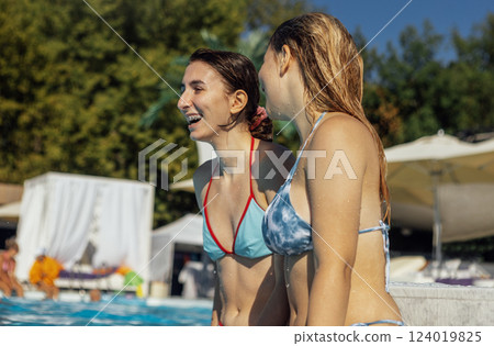 Two charming female friends are having fun in the pool. Smiling teenagers in swimsuits enjoy relaxing in the clear water. 124019825