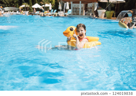 A little girl with an inflatable circle in the shape of a duck jumps into the pool. 124019838