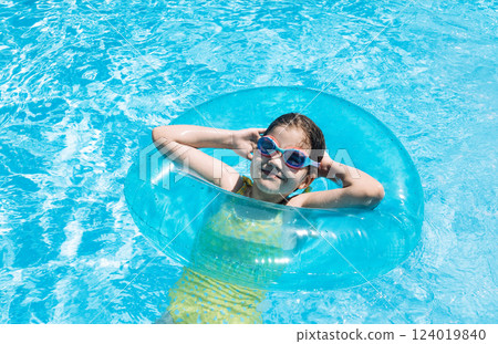 A little girl with an inflatable circle jumped into the pool. A cute kid in a swimsuit and swimming glasse 124019840
