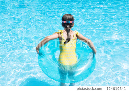 A little girl with an inflatable circle jumped into the pool. A cute kid in a swimsuit A little girl with an inflatable circle jumped into the pool. A cute kid in a swimsuit 124019841