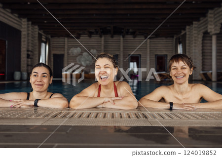Three young attractive women are laughing and having a great time in the pool. Female friends swim and enjoy the weekend together. 124019852