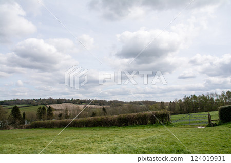 Fields, lawns and winter foliage seen from a hilltop under a cloudy sky in the Valley of the Ouse, outside London 124019931