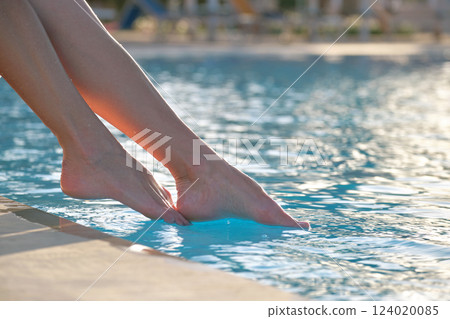 Young slim woman's legs relaxing near swimming pool in summer sun. Tropical vacation concept Young slim woman's legs relaxing near swimming pool in summer sun. Tropical vacation concept 124020085