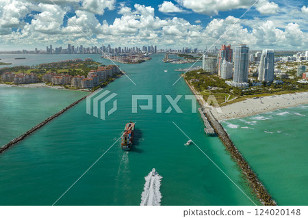 View from above of big container ship entering main channel in Miami harbor near South Beach high luxurious hotels and apartment buildings 124020148