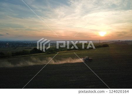 Tractor spraying fertilizers with insecticide herbicide chemicals on agricultural field at sunset 124020164
