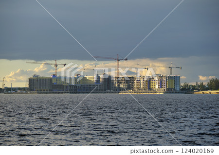 Tower cranes and frame structure of high residential apartment buildings at construction site on sea bay shore. Real estate development at waterfront Tower cranes and frame structure of high residential apartment buildings at construction site on sea bay shore. Real estate development at waterfront 124020169