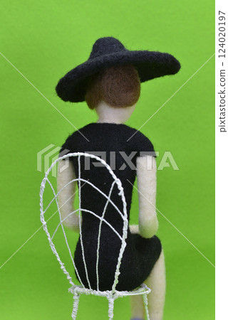 A female doll wearing a hat and sitting on a chair photographed from behind 124020197