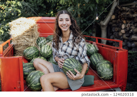 Charming smiling woman in casual clothes tosses watermelon outdoors 124020318