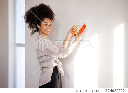 A beautiful smiling African woman in casual clothes holds color palettes. A charming young girl of mixed race chooses the color of the walls of the house. 124020322