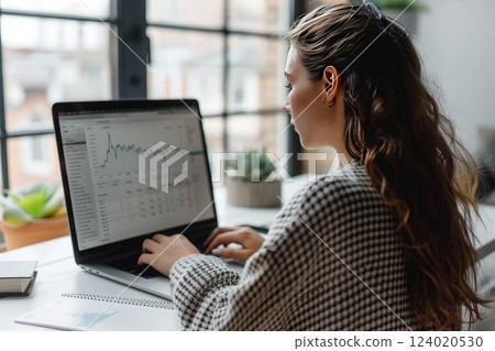 A woman is seated comfortably at a desk, working on a laptop computer. 124020530