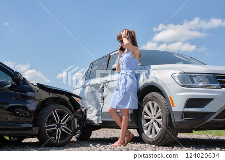 Sad female driver speaking on sellphone on street side calling for emergency service after car accident. Road safety and insurance concept 124020634