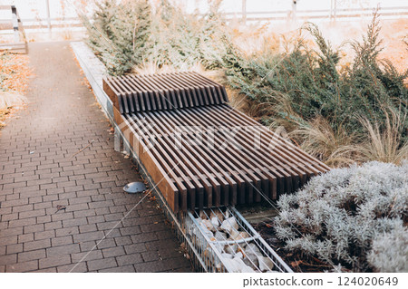 A modern wooden bench standing in the park. Comfortable bench in recreation area. City improvement, urban planning, public spaces. A modern wooden bench standing in the park. Comfortable bench in recreation area. City improvement, urban planning, public spaces. 124020649