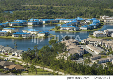 Protective tarp covering rooftop after hurricane damage against rain water leaking until replacement of asphalt shingles on damaged apartment buildings. Aftermath of natural disaster 124020671