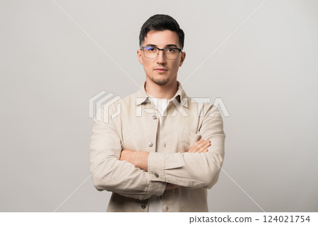 Unstoppable confidence. A man in eyeglasses and a beige overshirt standing with arms crossed, exuding self-assurance. A perfect blend of intellect and bold style 124021754