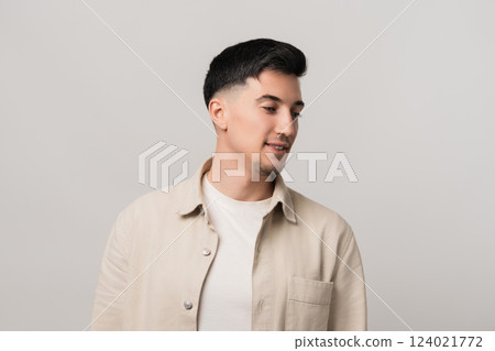 Earphones mockup blending fashion and tech. Stylish man in a beige overshirt gazing downward with a thoughtful expression, captured in a modern studio setting 124021772