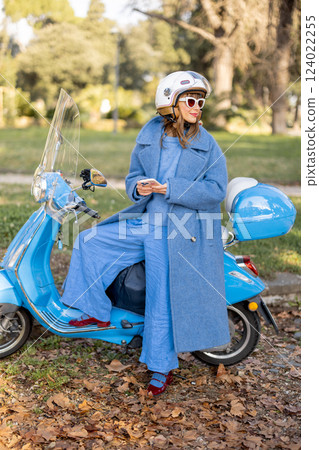 Elegant Woman Checking Phone Near Scooter in Park 124022255