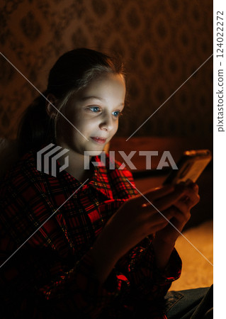 Vertical shot of cute preteen girl with vibrant blue eyes browsing smartphone screen, bathed in nocturnal digital light, expressing pure digital engagement and youthful happiness, close-up. Vertical shot of cute preteen girl with vibrant blue eyes browsing smartphone screen, bathed in nocturnal digital light, expressing pure digital engagement and youthful happiness, close-up. 124022272