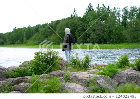girl in warm clothes stands on the shore of a mountain lake. girl in warm clothes stands on the shore of a mountain lake. 124022483