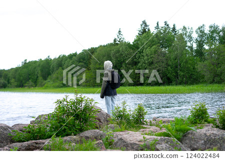 girl in warm clothes stands on the shore of a mountain lake. girl in warm clothes stands on the shore of a mountain lake. 124022484