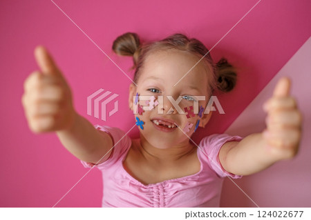 A child with multicolored puzzles adorning cheeks shows a thumbs-up sign with two hands. Awareness about autism. A child with multicolored puzzles adorning cheeks shows a thumbs-up sign with two hands. Awareness about autism. 124022677