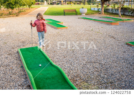 Little girl playing mini golf outdoor. Child having fun with new activity in spring time. Family vacations or resort. Little girl playing mini golf outdoor. Child having fun with new activity in spring time. Family vacations or resort. 124022758