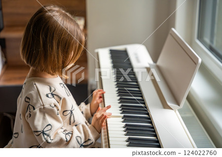 Home lesson on music for the girl on white piano synthesizer. Concept of early development: learning music enhances motor skills, hearing, and intelligence, fostering creativity from childhood 124022760