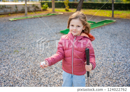 Portrait of Little girl Holding in hand Mini-Golf Ball. Little girl playing mini golf outdoor. Family vacations or resort. 124022762