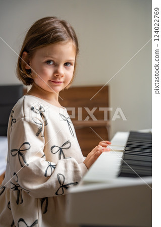 Home lesson on music for the girl on white piano synthesizer. Concept of early development: learning music enhances motor skills, hearing, and intelligence, fostering creativity from childhood 124022769