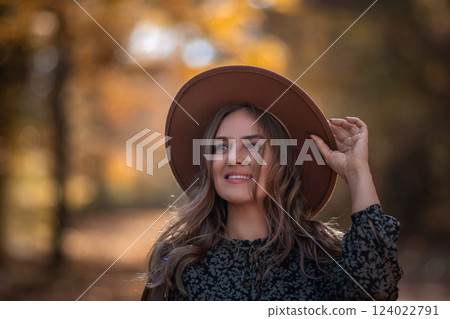Woman Hat Autumn Portrait: Smiling girl adjusts hat outdoors during fall foliage photoshoot. Woman Hat Autumn Portrait: Smiling girl adjusts hat outdoors during fall foliage photoshoot. 124022791