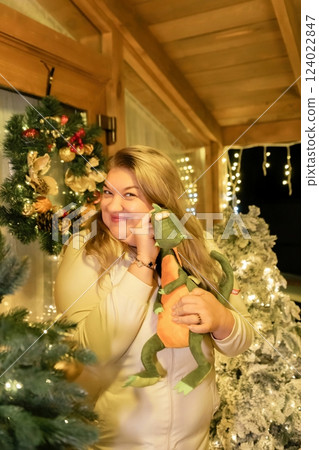 Woman Christmas Tree Phone Call - A woman in a white sweater smiles while holding a stuffed toy and talking on the phone in front of a decorated Christmas tree. Woman Christmas Tree Phone Call - A woman in a white sweater smiles while holding a stuffed toy and talking on the phone in front of a decorated Christmas tree. 124022847