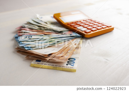 Pile of various value Euro banknotes money spread on the table with an orange calculator on the cash Pile of various value Euro banknotes money spread on the table with an orange calculator on the cash 124022923